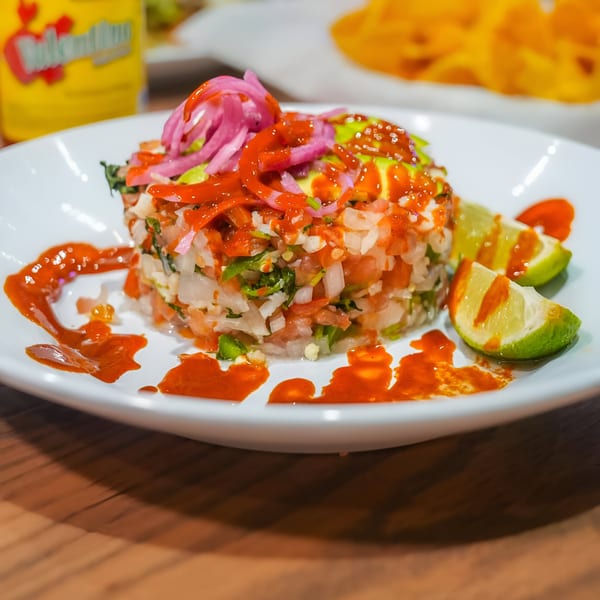 Mexican ceviche with red sauce, pickled onions, and lime wedges on a white plate.