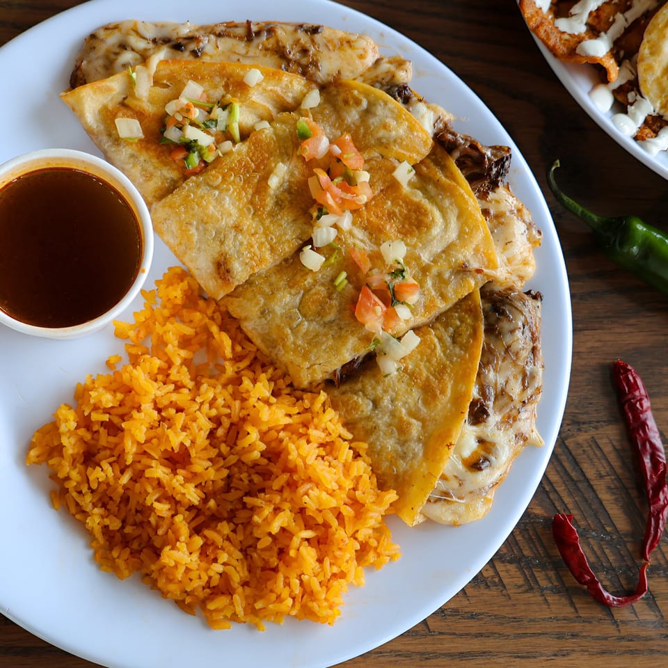 A plate of cheesy quesadillas topped with pico de gallo, served with rice and dipping sauce.