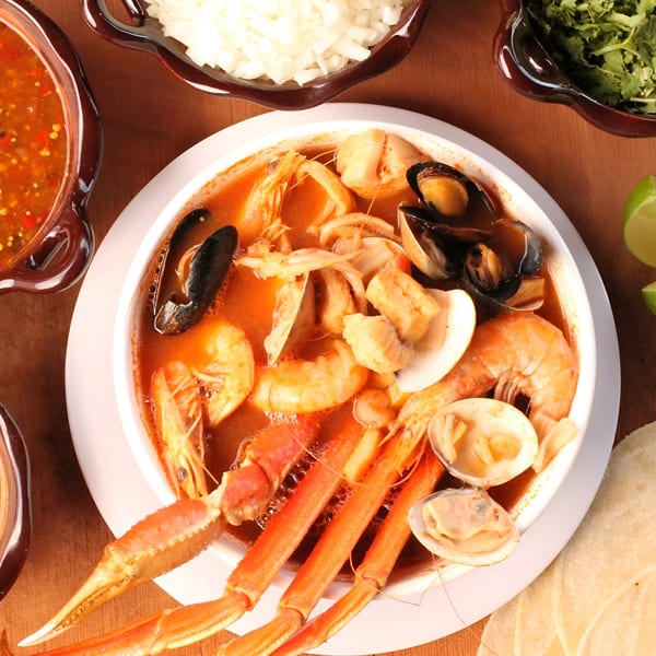 Overhead view of a large bowl of Mexican seafood soup with crab legs, shrimp, mussels, and clams.