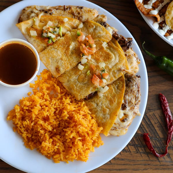 A plate of cheesy quesadillas topped with pico de gallo, served with rice and dipping sauce.