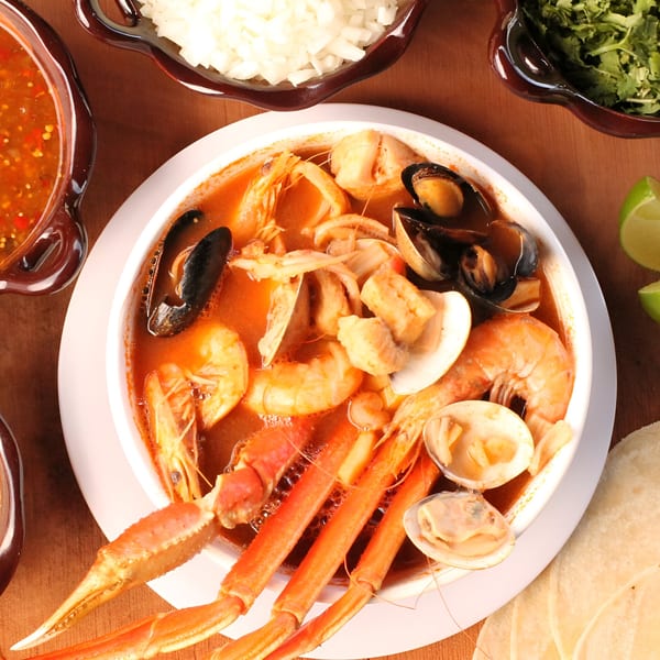Overhead view of a large bowl of Mexican seafood soup with crab legs, shrimp, mussels, and clams.