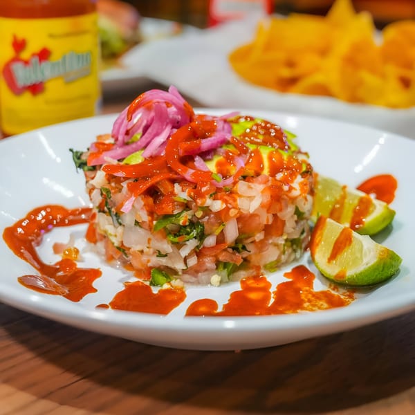 Taqueria Los Portales' ceviche with red sauce, pickled onions, and lime wedges on a white plate.