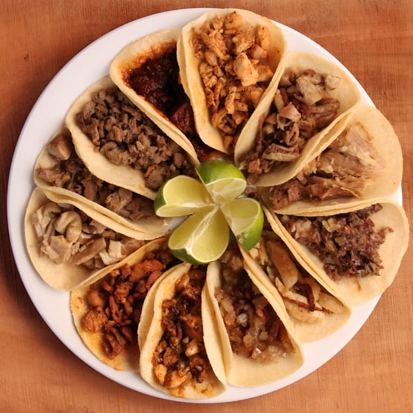 A white plate filled with a variety of Mexican street tacos, garnished with lime wedges.