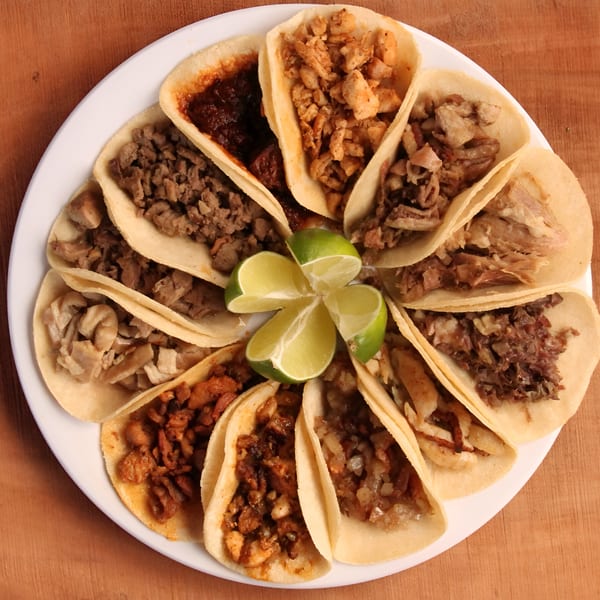 A white plate filled with various Taqueria Los Portales tacos, garnished with lime wedges.
