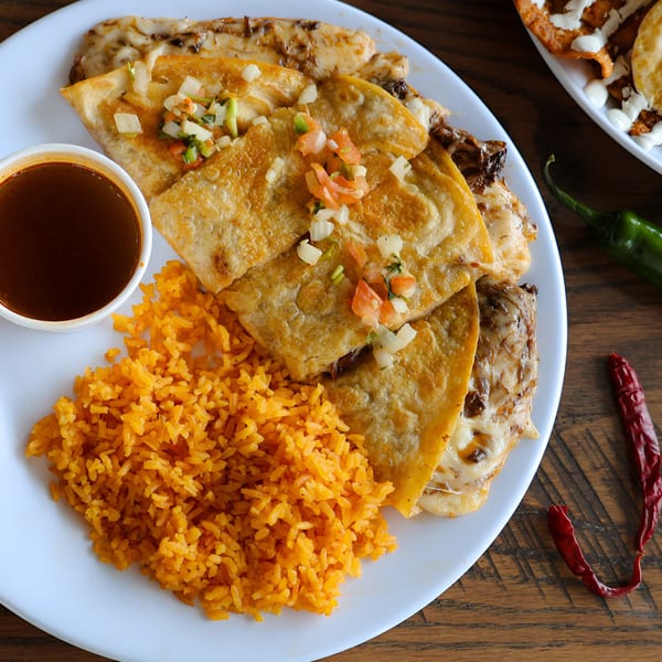 Quesadillas topped with pico de gallo, served with Mexican rice and a side of dipping sauce.